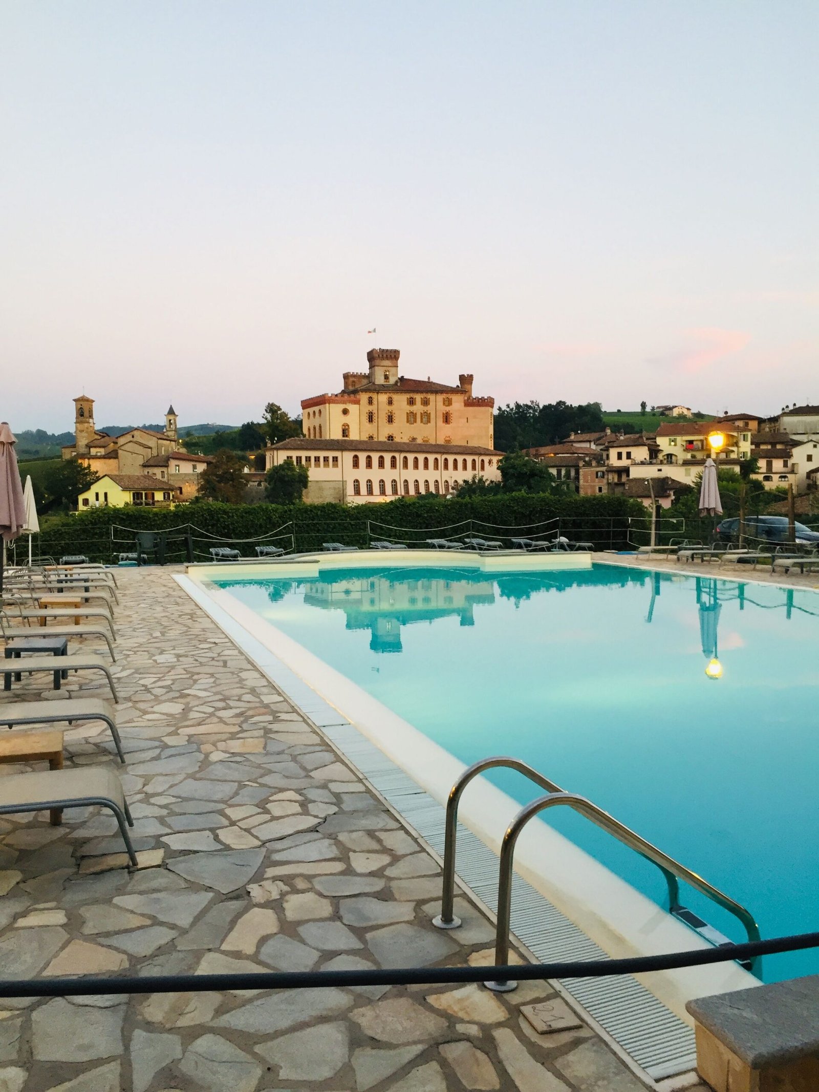 Experience luxury with a stunning poolside view of Barolo, Italy, capturing the serene ambiance at dusk.