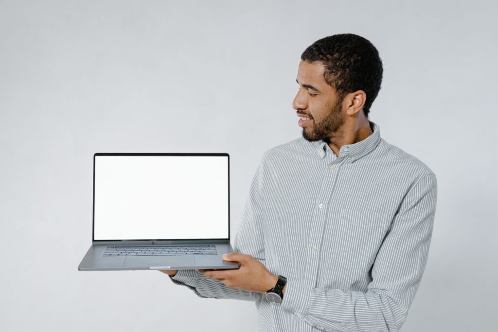 Man in striped shirt showcasing a laptop with blank screen against white background.